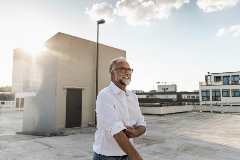 Mature Man Standing On Roof Of A High Rise Building, Rolling Up Sleeves